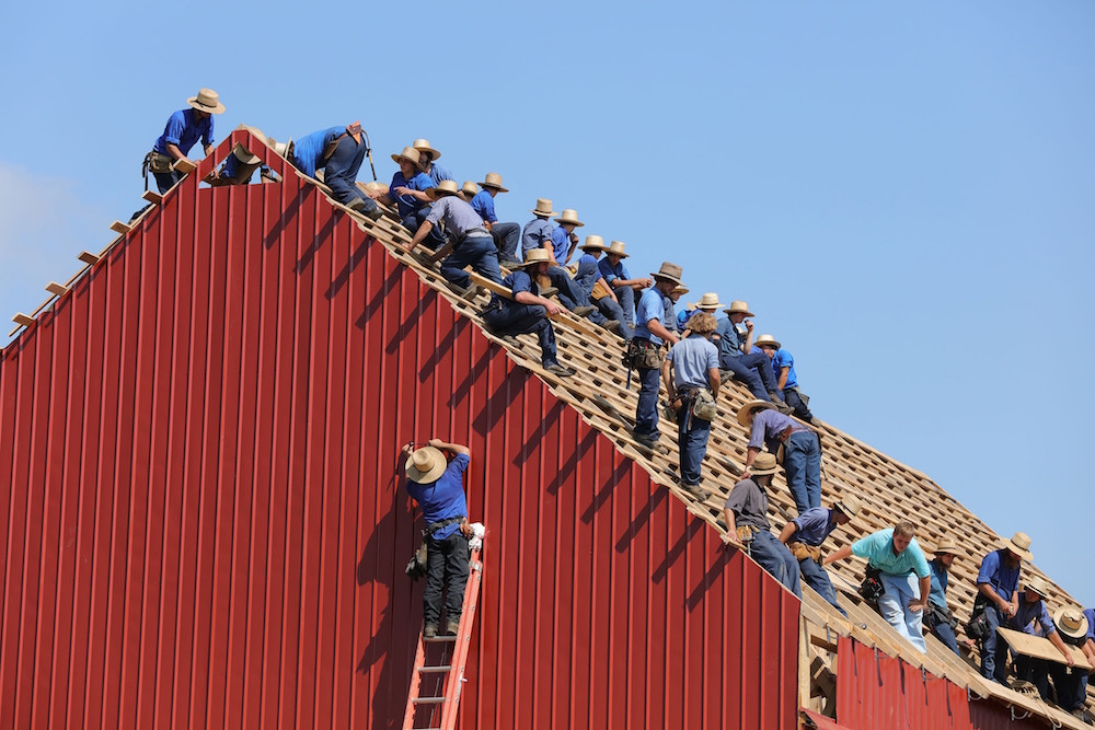 A group of hard working men in the process of completing the roof of red a steel horse barn for a ranch owner 